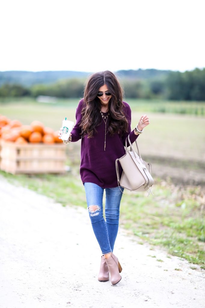 Девушка рядом с тыквами в фиолетовом удлиненном свитере и в джинсах