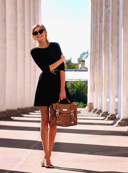 Модель в черном платье с ремешком на талии и коричневой сумкой