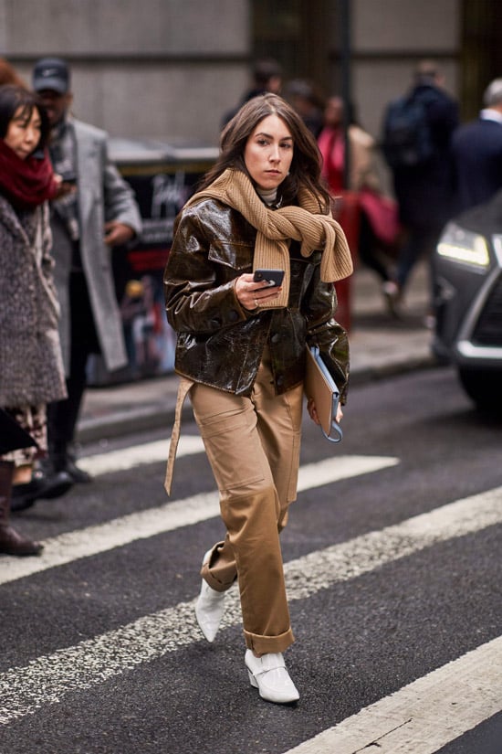 Девушка в бежевых брюках, кожаная куртка и вязанный свитер на шее