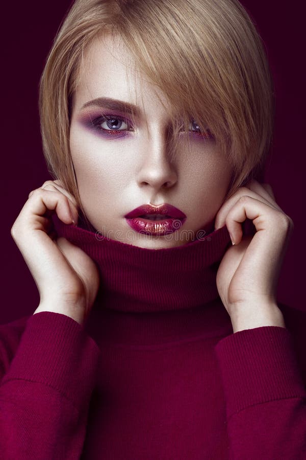 Beautiful blonde woman in a red sweater with bright makeup and dark lips. Beauty face. Beauty face. Picture taken in the studio royalty free stock image