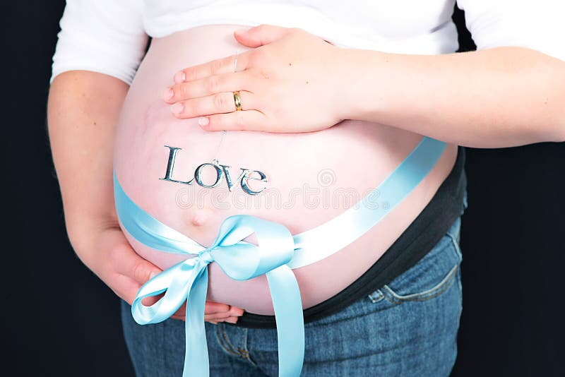 Blue bow around pregnant woman. Blue ribbon tied in bow around stomach of pregnant woman with word love, black background royalty free stock images