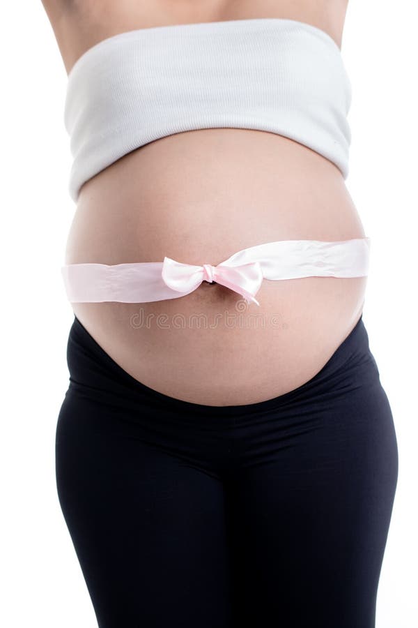 Pink ribbon bow over the pregnant woman`s belly. Close-up of pink ribbon bow over the pregnant woman`s belly against white background stock photo