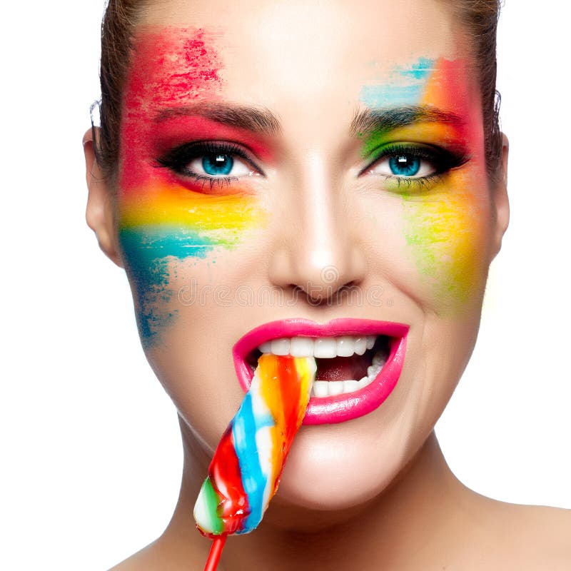 Fantasy Makeup. Painted Face. Lollipop. Beautiful young woman with fantasy makeup eating a colorful lollipop looking at camera. Beauty and makeup concept royalty free stock photo