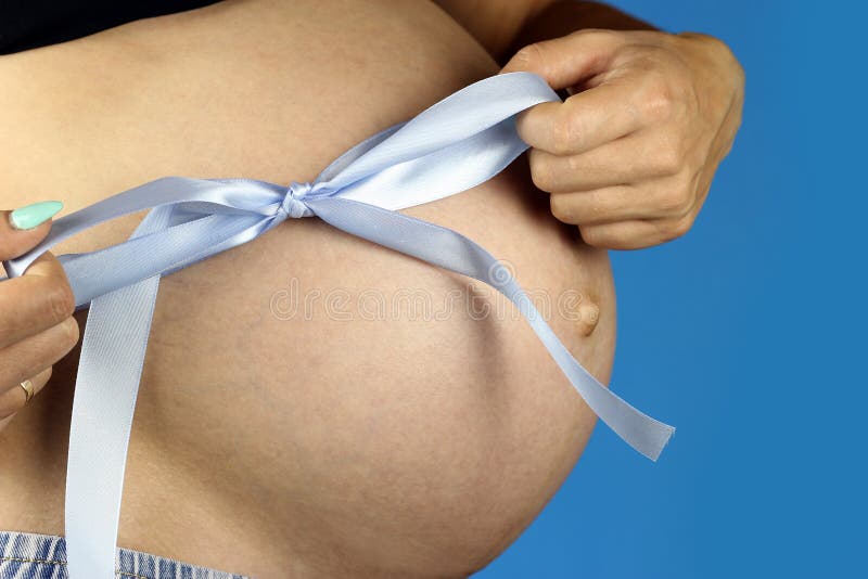 Girl ties a blue bow on a pregnant belly.  royalty free stock photos