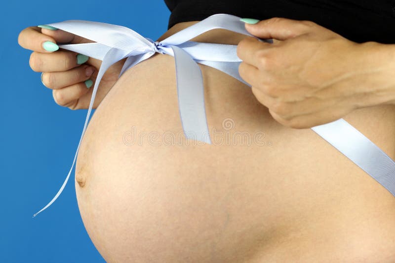 Girl ties a blue bow on a pregnant belly.  royalty free stock photography
