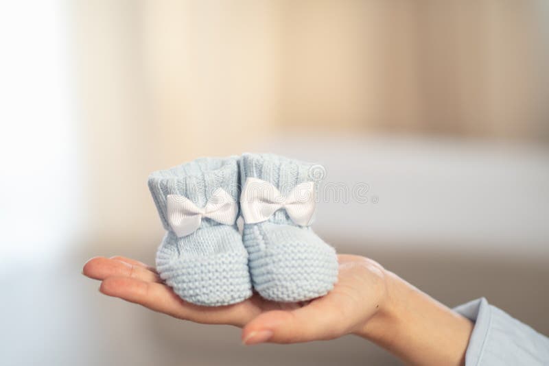 Little blue knitted socks with a bow on the hand of pregnant woman. Pregnancy and parenthood concept.  royalty free stock photography