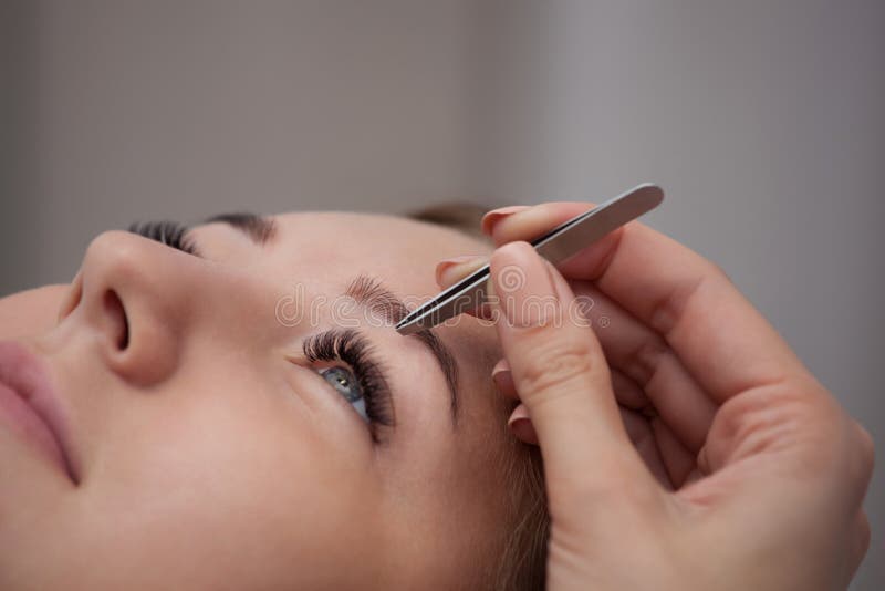Master makeup corrects, and gives shape to pull out with forceps previously painted with henna eyebrows in a beauty salon. Professional care for face royalty free stock photo