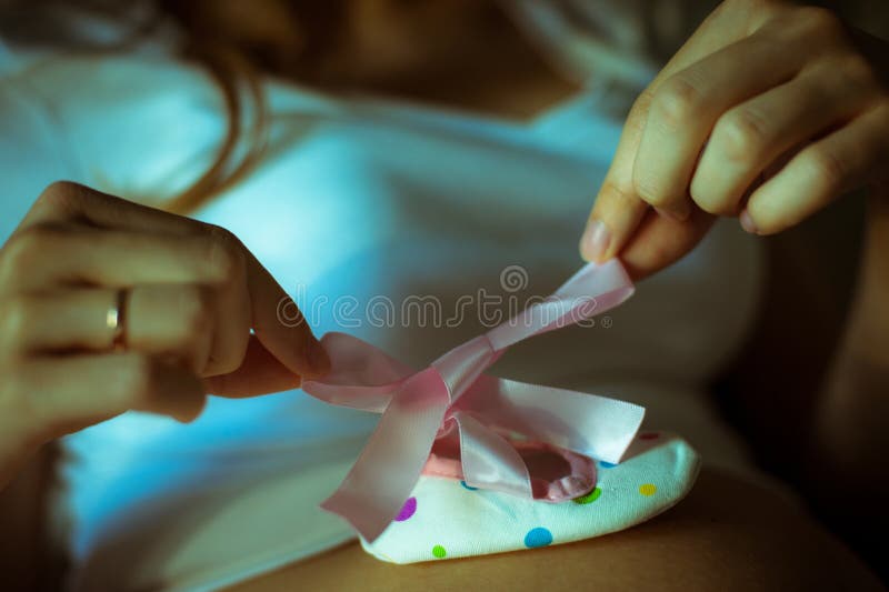 A pregnant woman holding white shoe and pink bow. Ribbon on pregnancy belly. Waiting for daughter stock photography
