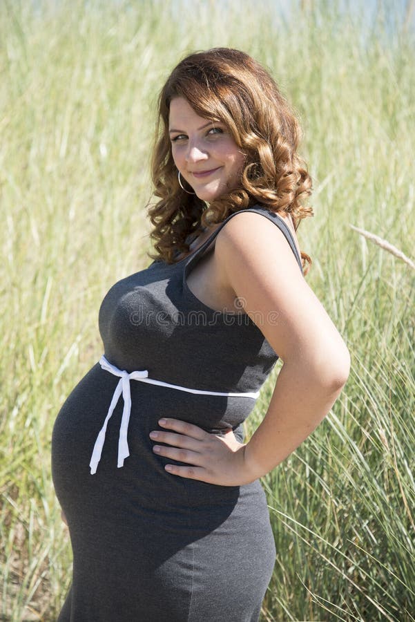 Pregnant woman with white ribbon bow. On her belly in nature with straw background stock photos