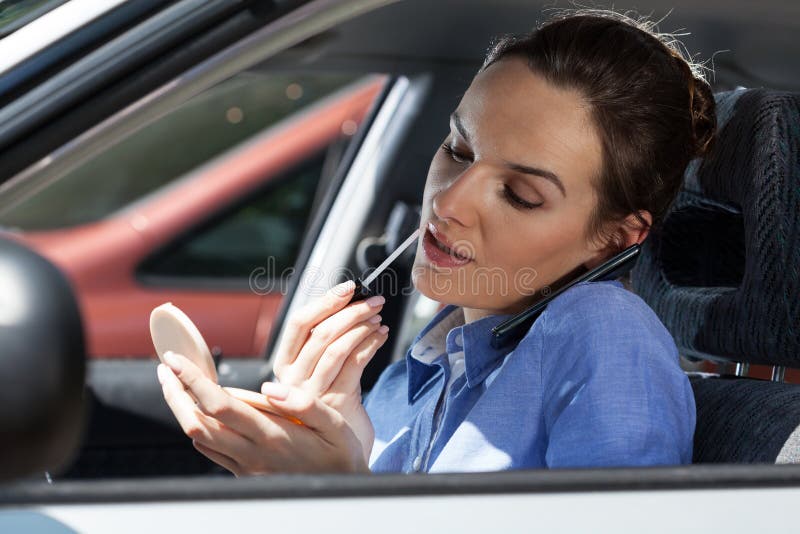 Pretty woman in a car doing makeup while standing in a traffic jam. Pretty woman in a car talking on phone and doing makeup while standing in a traffic jam stock photo