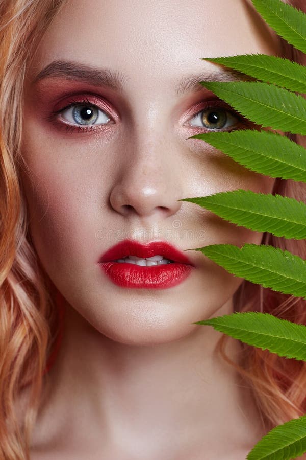 fashion blonde with bright red makeup and branch fern on bright red background. Girl with perfect figure. Professional makeup stock images