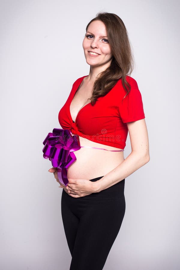 Thin pregnant girl in a red blouse with small tummy bandaged with a bow. Thin pregnant girl in a red blouse with a small tummy bandaged with a bow stock photo