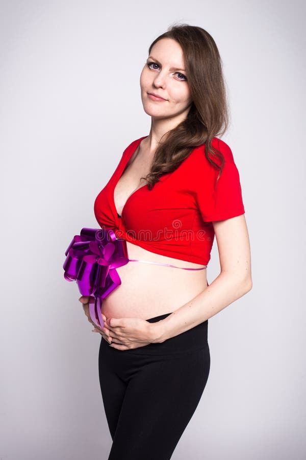 Thin pregnant girl in a red blouse with small tummy bandaged with a bow. Thin pregnant girl in a red blouse with a small tummy bandaged with a bow stock images
