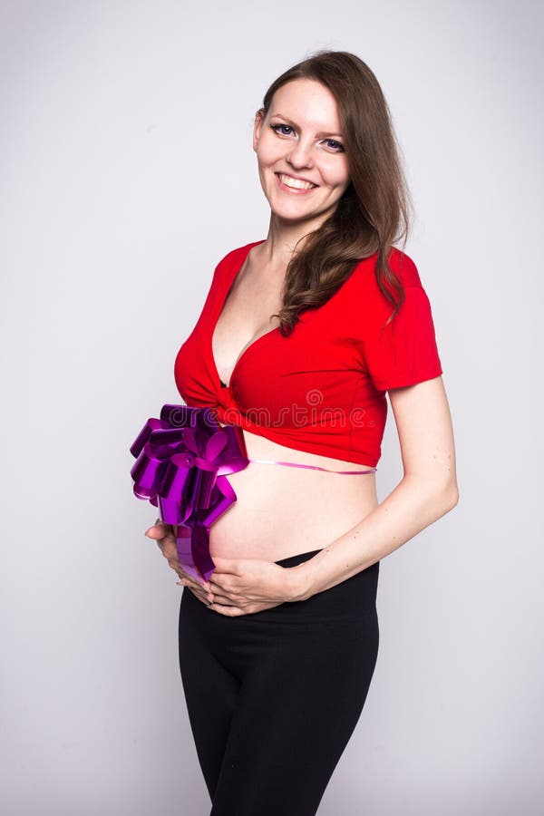 Thin pregnant girl in a red blouse with small tummy bandaged with a bow. Thin pregnant girl in a red blouse with a small tummy bandaged with a bow stock photos