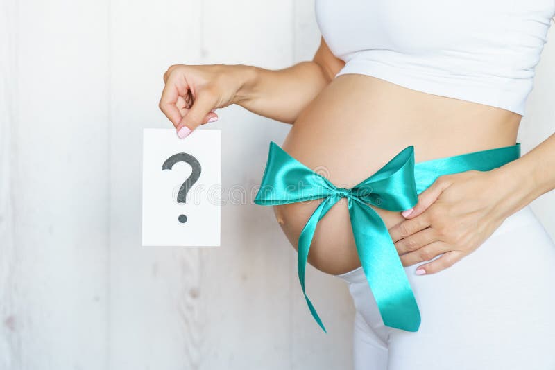 Tummy with green ribbon and bow of pregnant caucasian woman which is holding question. In light room royalty free stock photos