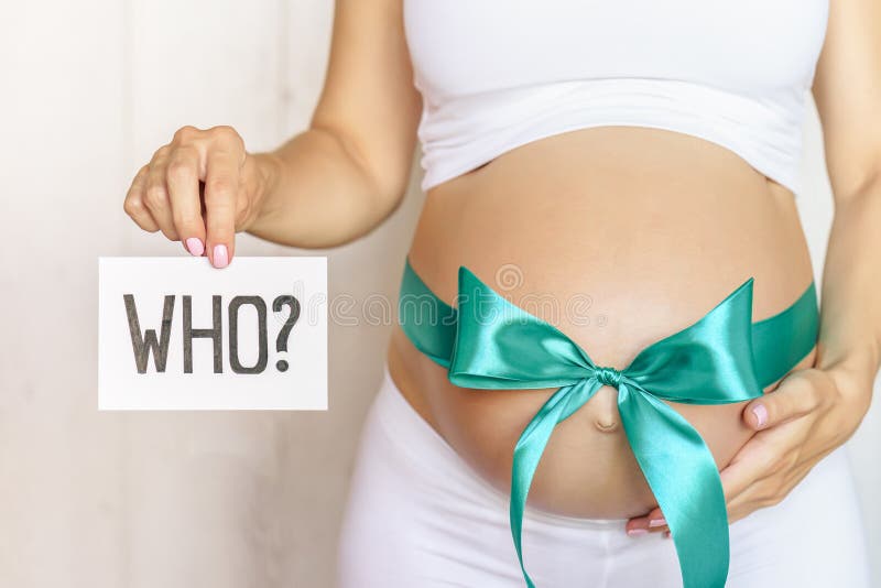 Tummy with green ribbon and bow of pregnant caucasian woman which is holding question. In light room royalty free stock image
